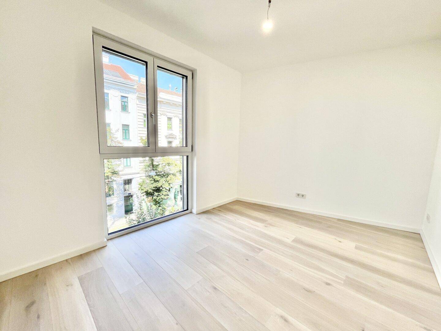 Heller, leerer Raum mit Holzboden und einem großen Fenster, das einen Blick ins Grüne ermöglicht.