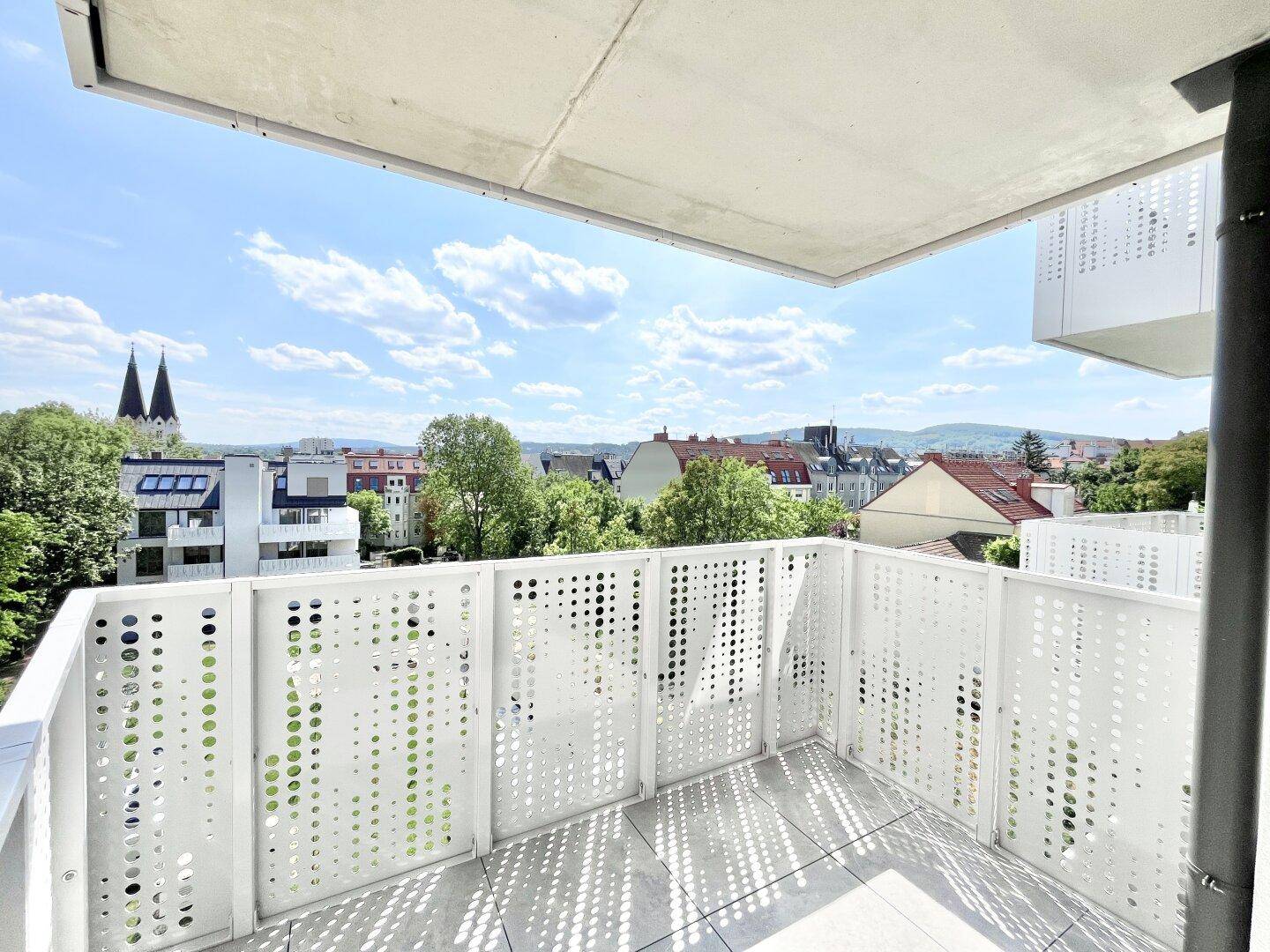 Geräumiger Balkon mit moderner Lochblechverkleidung und weitem Blick über die Stadt und grüne Umgebung.