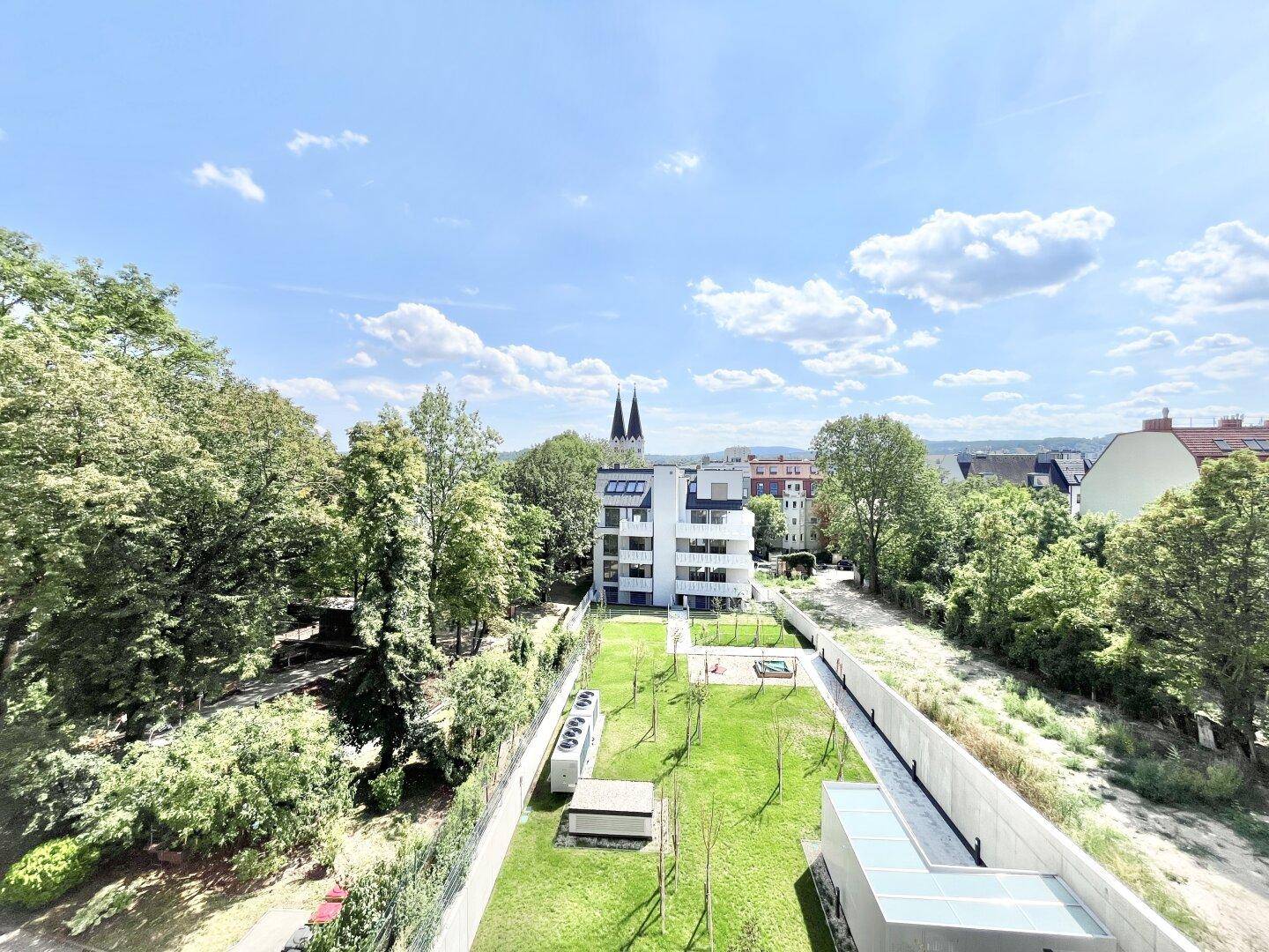 Luftaufnahme eines modernen Wohnkomplexes mit gepflegtem Innenhof und Blick auf die Stadt.