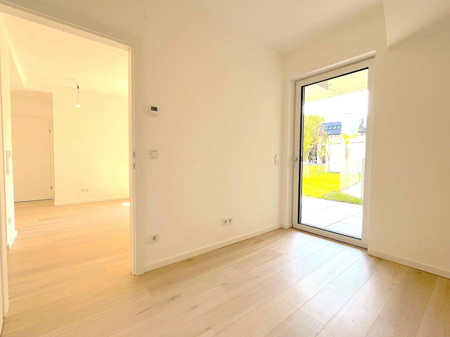 Ein heller Raum mit Holzboden und einer großen Glastür, die Zugang zum Außenbereich bietet.