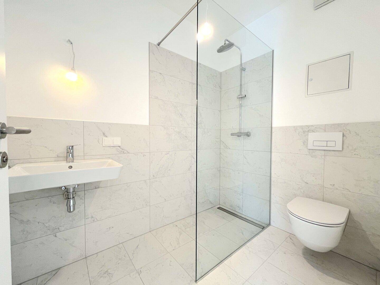 Ein modernes Badezimmer mit weißen Marmorfliesen, einer begehbaren Dusche und einem wandmontierten WC.
