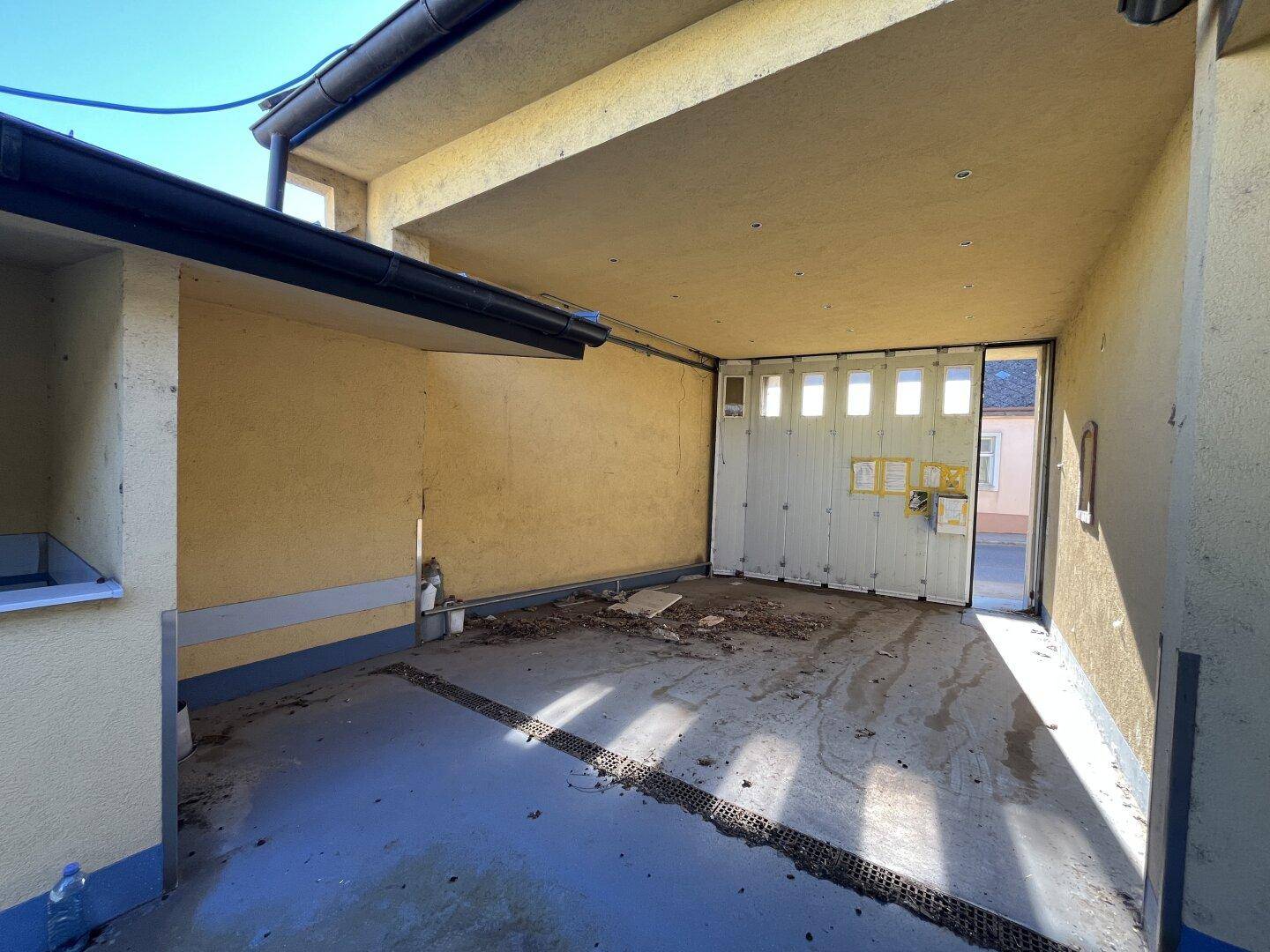 Überdachter Garagenbereich mit einem großen Tor und Entwässerungsrinnen im Boden.