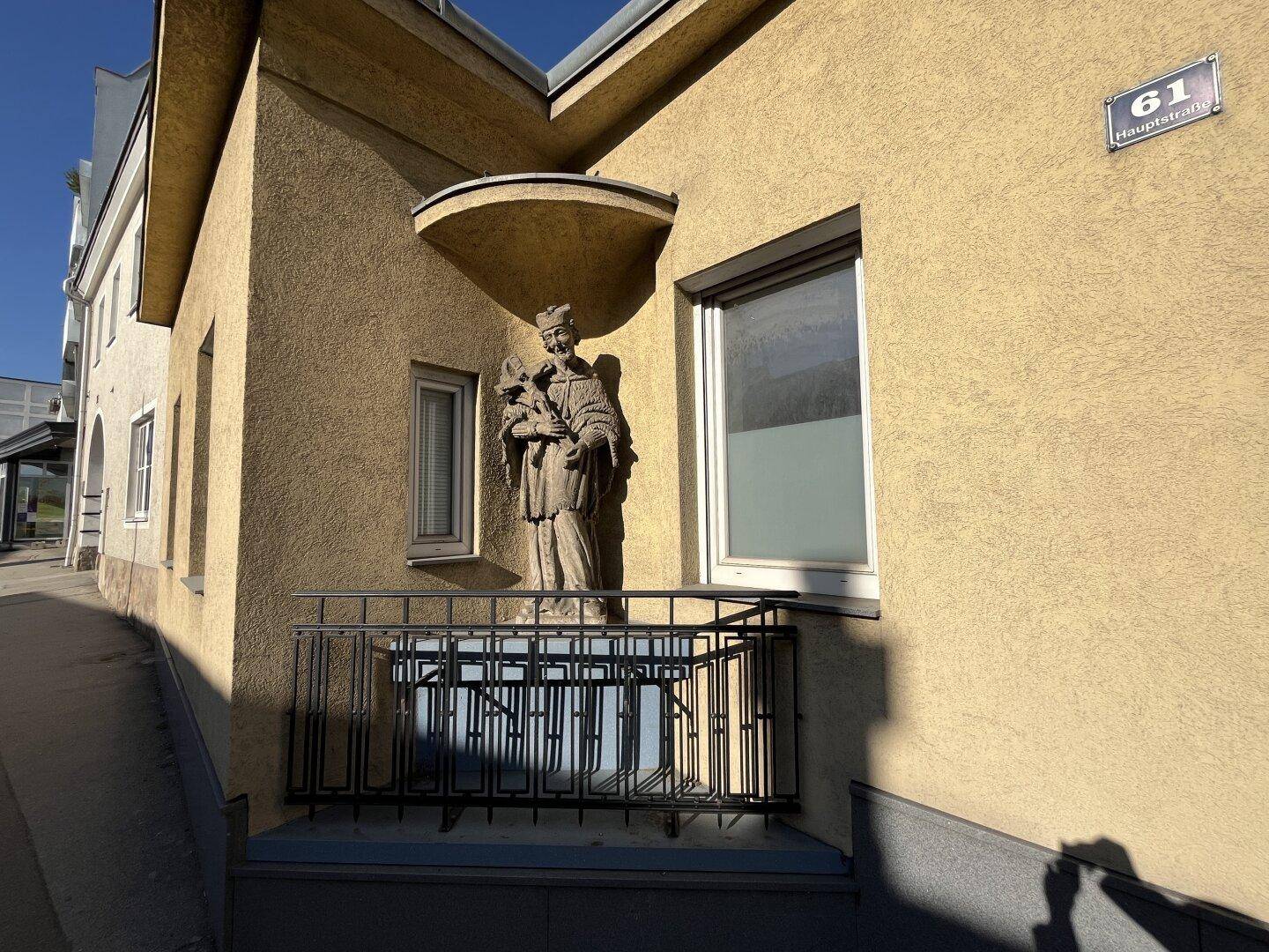 Detailansicht der Hausfassade mit einer religiösen Statue auf einem kleinen Balkon und Hausnummernschild.