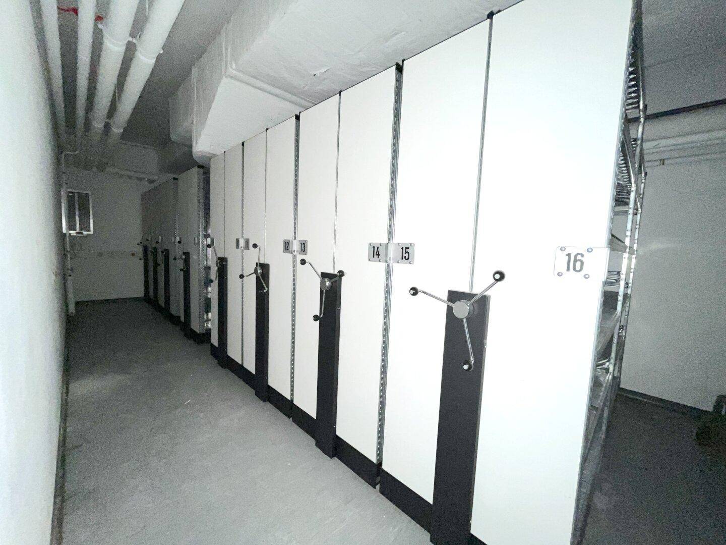 Lagerraum mit einer Reihe von mobilen Archivregalen und sichtbaren Deckeninstallationen in einem funktionalen Bereich.