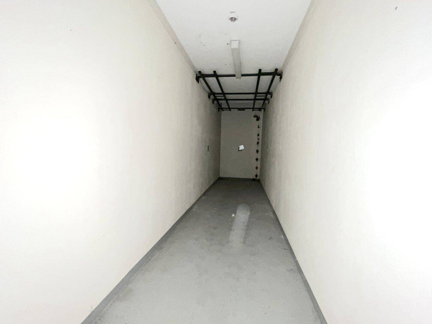 Leerer, langer Korridor mit weißen Wänden und einer sichtbaren Deckeninstallation.