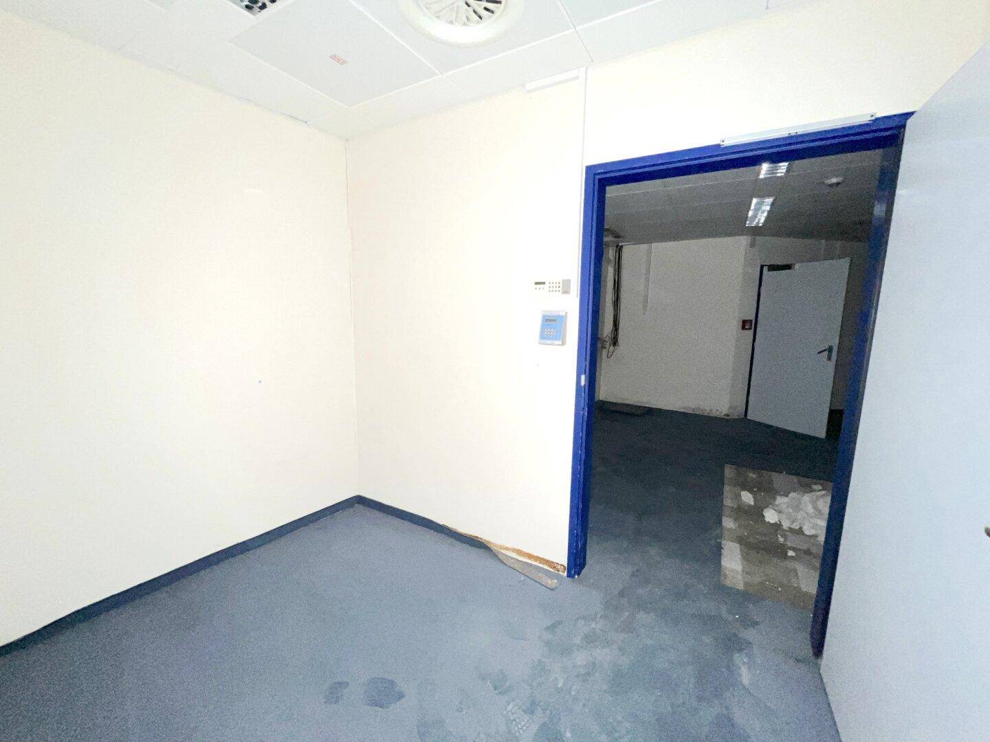 Kleiner Büroraum mit blauer Teppichboden und weiß gestrichenen Wänden, bereit zur Nutzung.