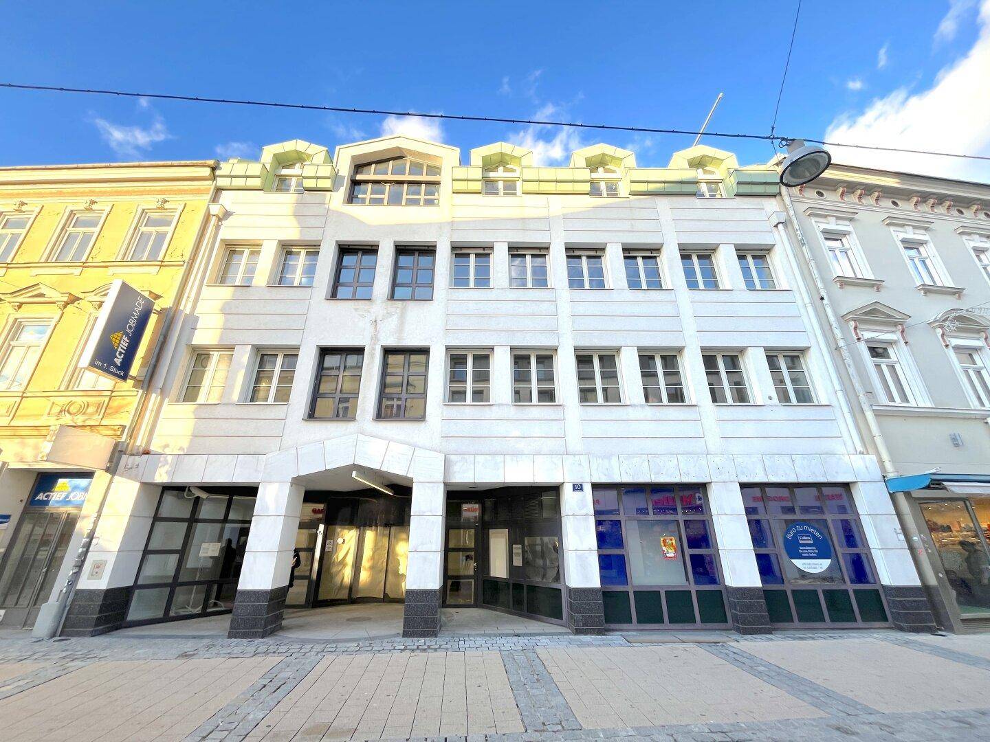 Mehrstöckiges Geschäftsgebäude mit weißer Fassade und großen Fenstern in einer Stadtstraße.