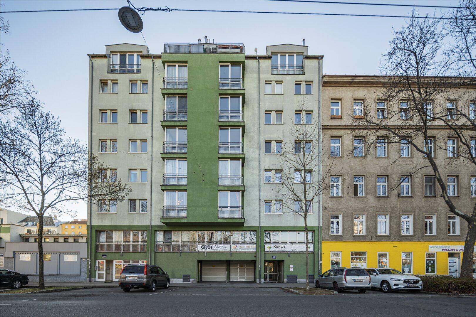 Mehrstöckiges Wohngebäude mit grüner Fassade, Balkonen und großen Fenstern.