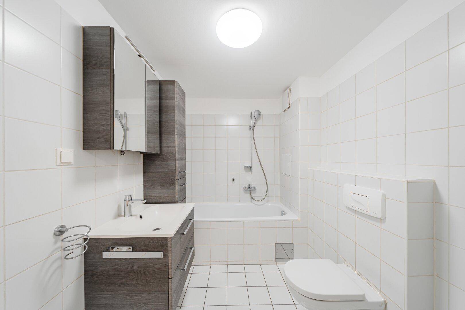 Modern gefliestes Badezimmer mit Badewanne, Toilette und Waschtischunterschrank.