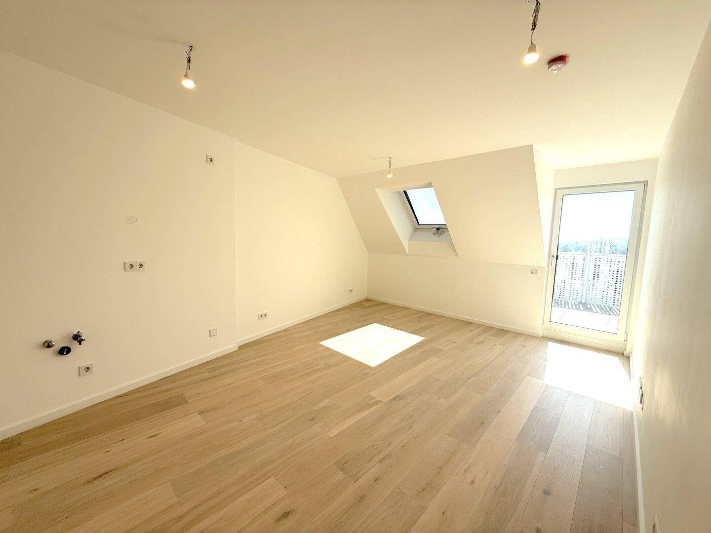 Geräumiger Dachgeschossraum mit hellem Holzfußboden, Dachfenster und Balkonzugang, mit Anschlüssen.