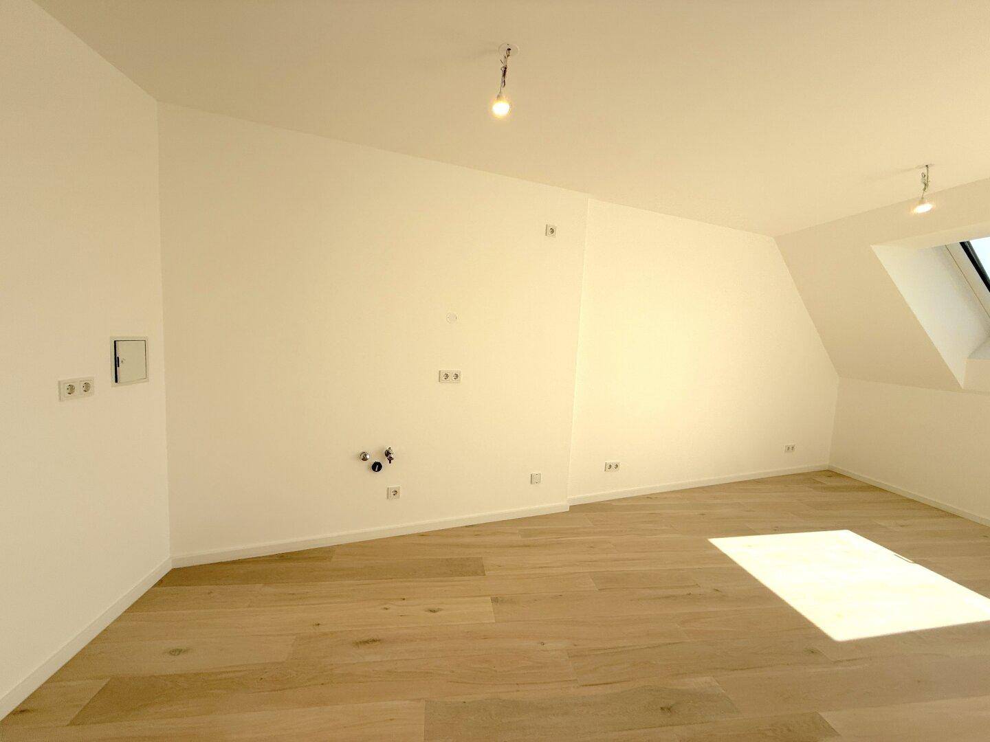 Heller Dachgeschossraum mit Holzfußboden, Dachfenster und Balkonzugang, vorbereitet für Kücheninstallationen.