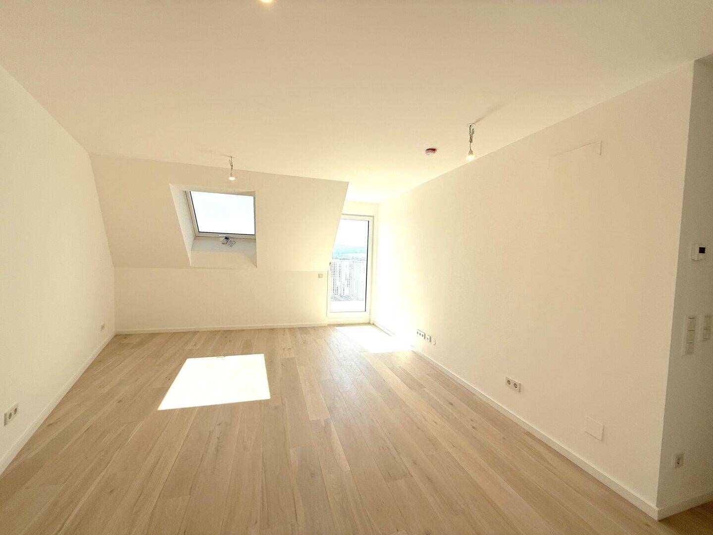 Lichtdurchfluteter Dachgeschossraum mit hellem Holzfußboden, Dachfenster und direktem Balkonzugang.