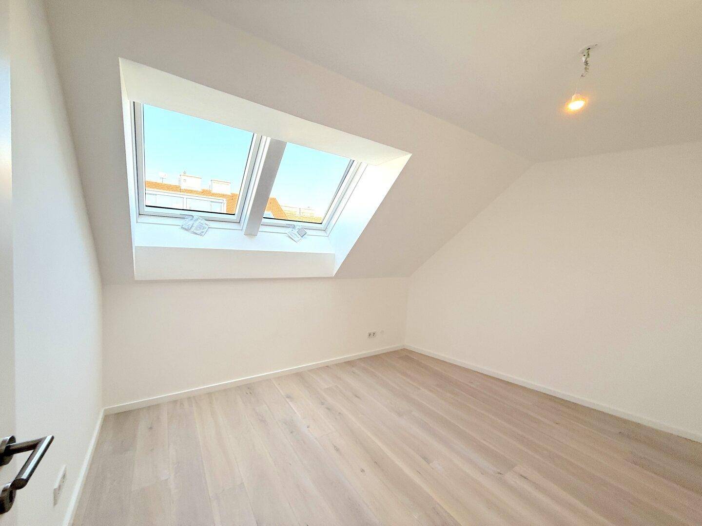 Heller Raum im Dachgeschoss mit schrägen Wänden und großem Dachfenster, ideal für ein Schlafzimmer.