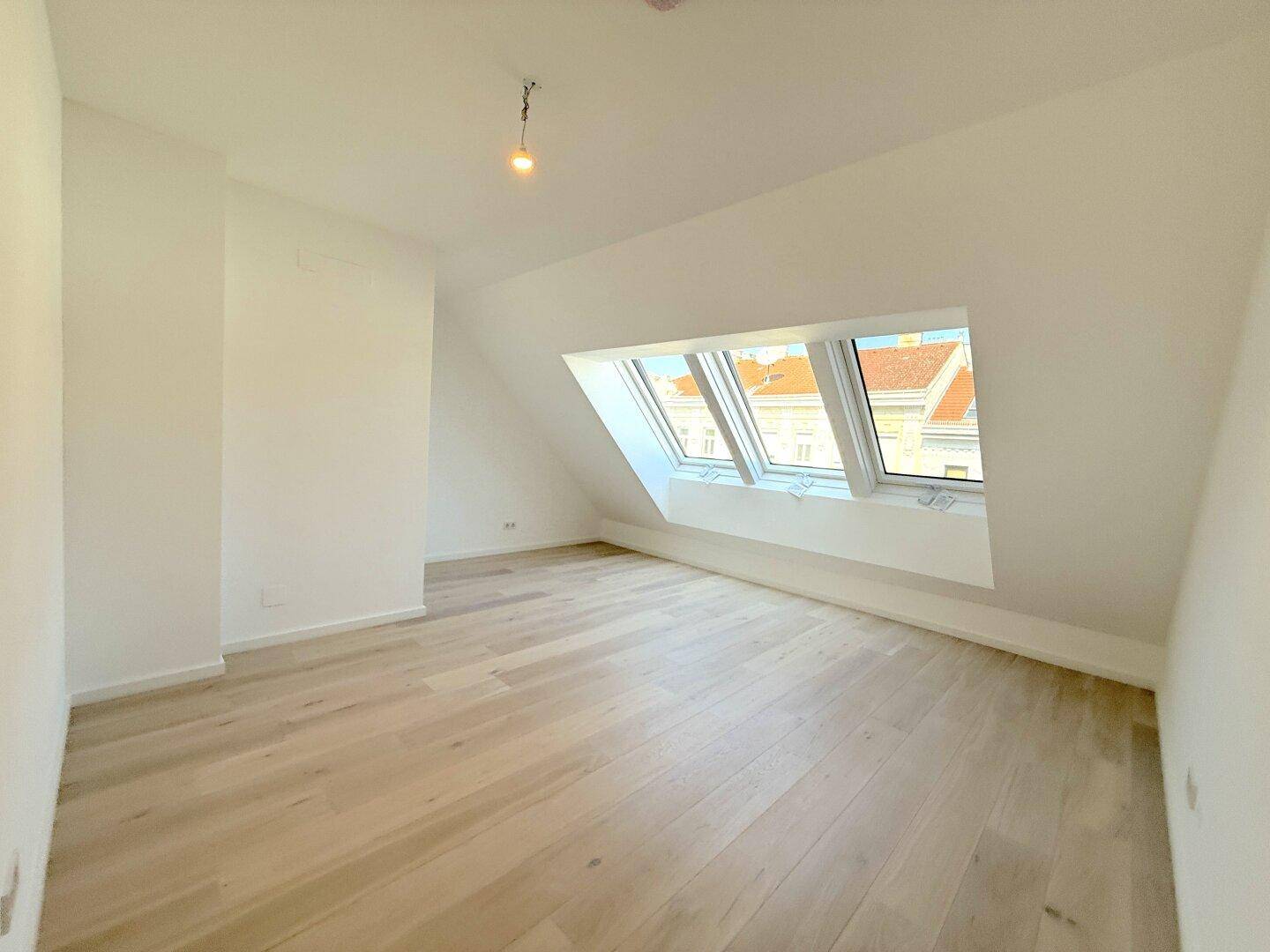 Lichtdurchfluteter Dachgeschossraum mit mehreren Dachfenstern und hellem Holzfußboden, bereit zum Einrichten.