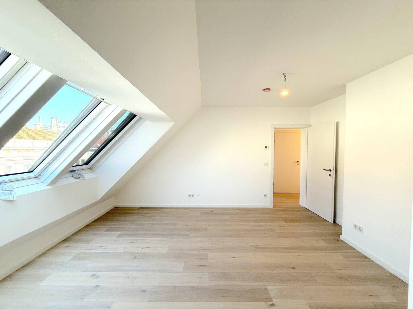 Großer, heller Dachgeschossraum mit schrägen Wänden, Dachfenstern und neuem Holzfußboden.
