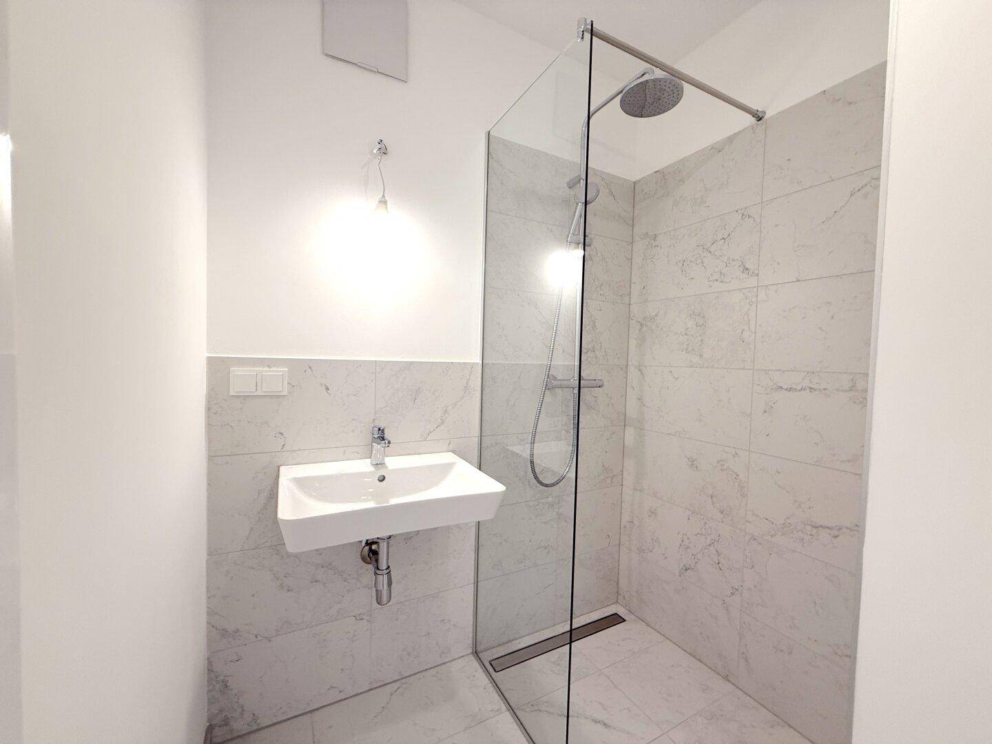 Helles Badezimmer mit moderner ebenerdiger Dusche, Wandwaschbecken und eleganten Marmorfliesen.