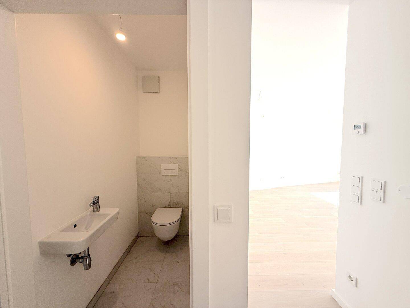Kompaktes Gäste-WC mit wandhängender Toilette, kleinem Waschbecken und modernen Fliesen.