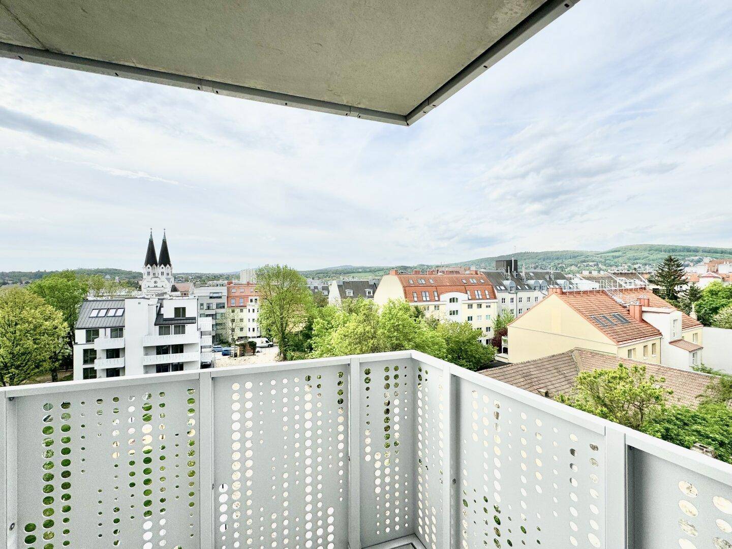 Balkon mit weitem Blick über die Stadt und die umliegende grüne Landschaft unter bewölktem Himmel.