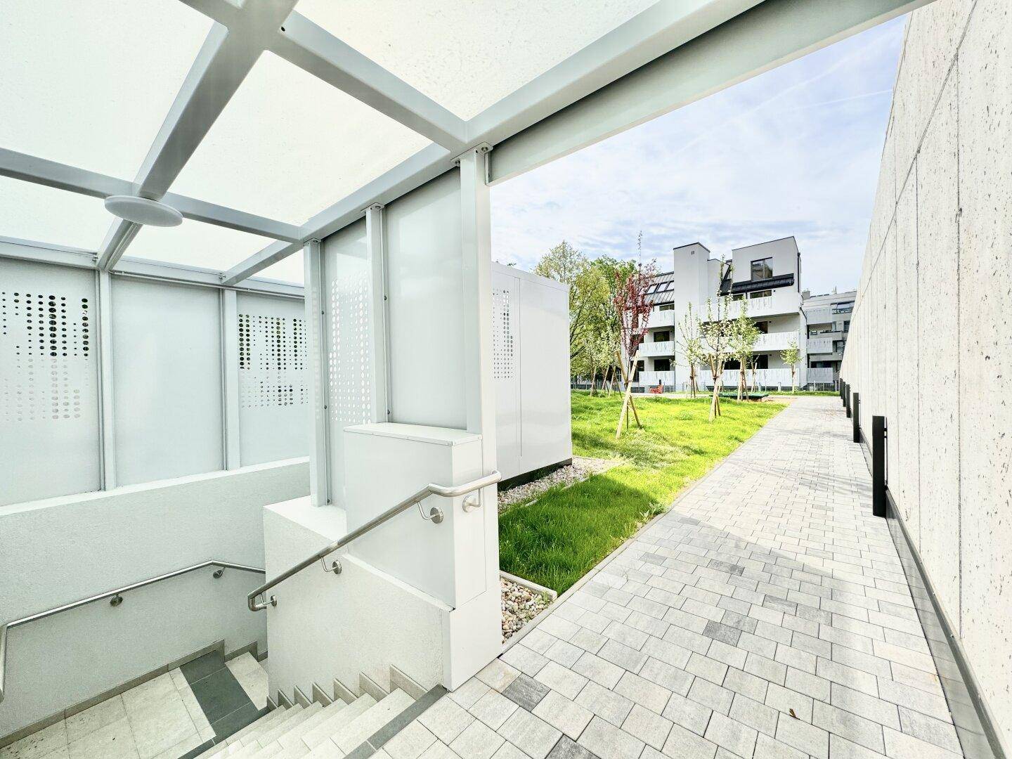 Moderner Zugang zu einem Untergeschoss mit Treppe und gepflastertem Weg neben der Wohnanlage.