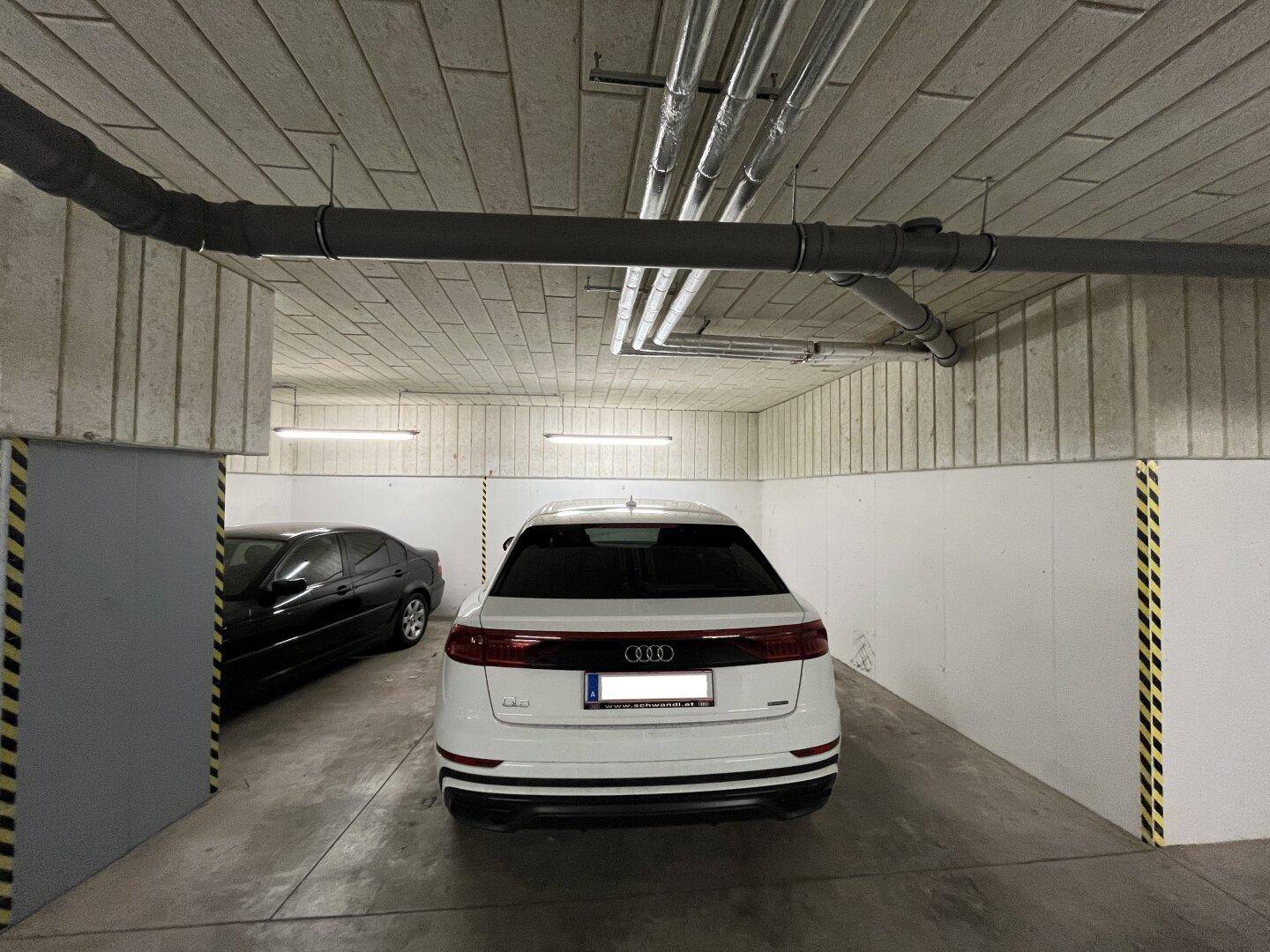 Ansicht einer Tiefgarage mit einem weißen Auto, Betonwänden und Deckeninstallationen.