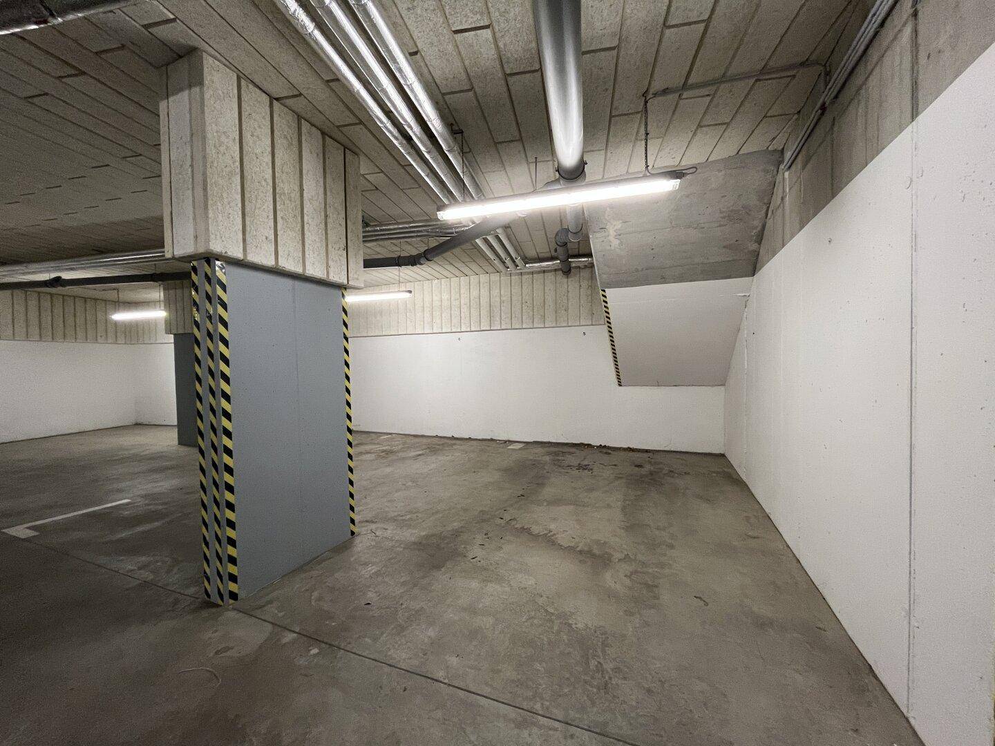 Leerer Stellplatz in einer Tiefgarage mit Betonpfeiler und sichtbaren Deckenstrukturen.