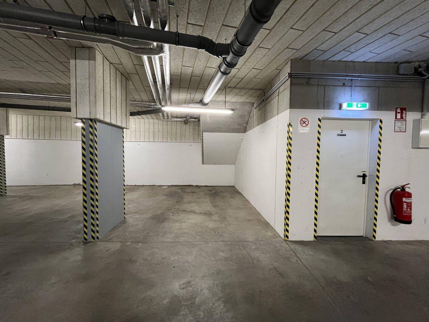 Leerer Stellplatz in der Tiefgarage mit einer Tür, Feuerlöscher und Betonpfeilern.