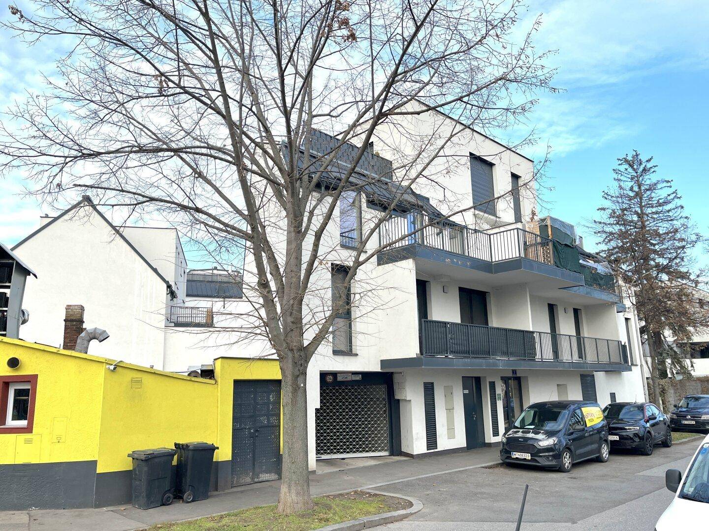 Modernes Mehrfamilienhaus mit Balkonen und geparkten Autos an einer Wohnstraße.