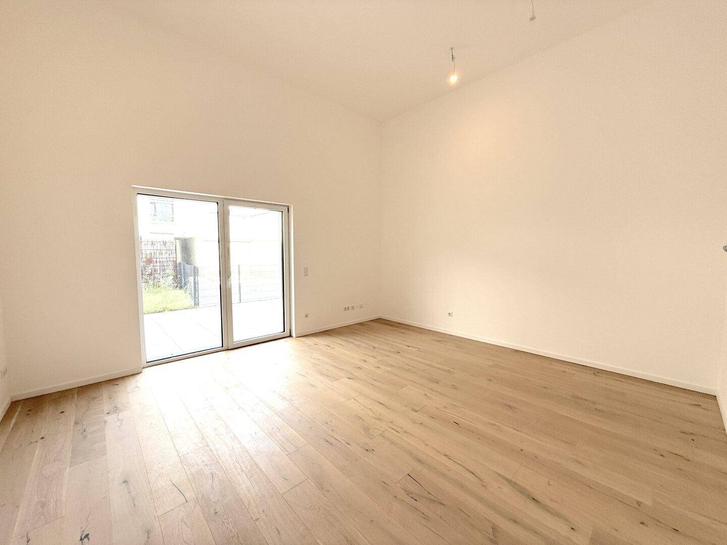 Geräumiger, heller Raum mit Holzboden, hohen Decken und großer Schiebetür zum Außenbereich.