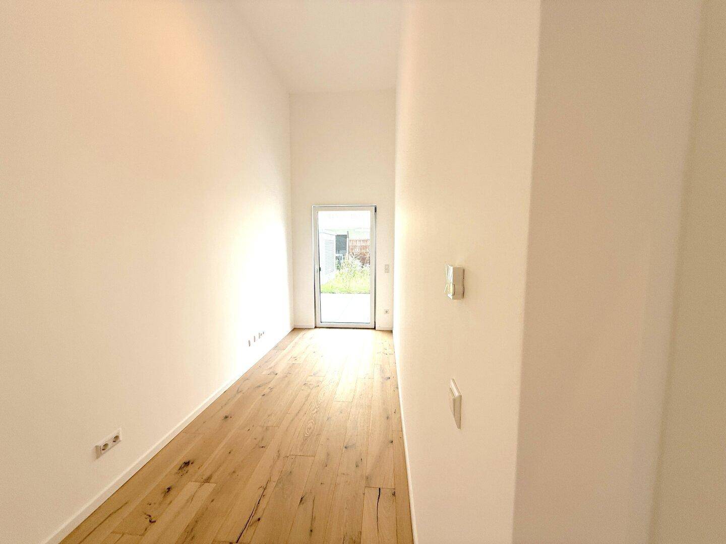 Heller Flur mit Holzboden und Ausgang zu einem sonnigen Außenbereich.