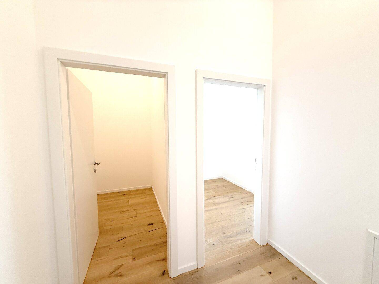 Heller Flur mit zwei offenen Türen zu weiteren leeren Räumen mit Holzboden.