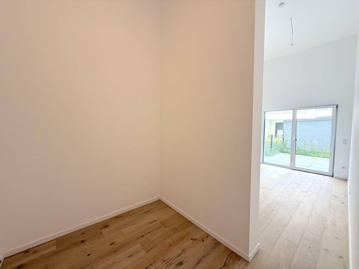 Kleiner, heller Raum mit Holzboden und Blick auf den Außenbereich durch eine Glasfront.