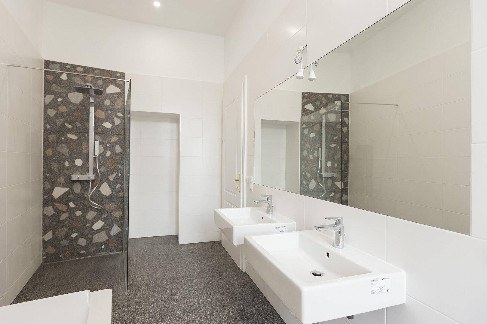 Modernes Badezimmer mit zwei Waschbecken, großer Spiegelfläche und einer begehbaren Dusche mit Terrazzo-Fliesen.