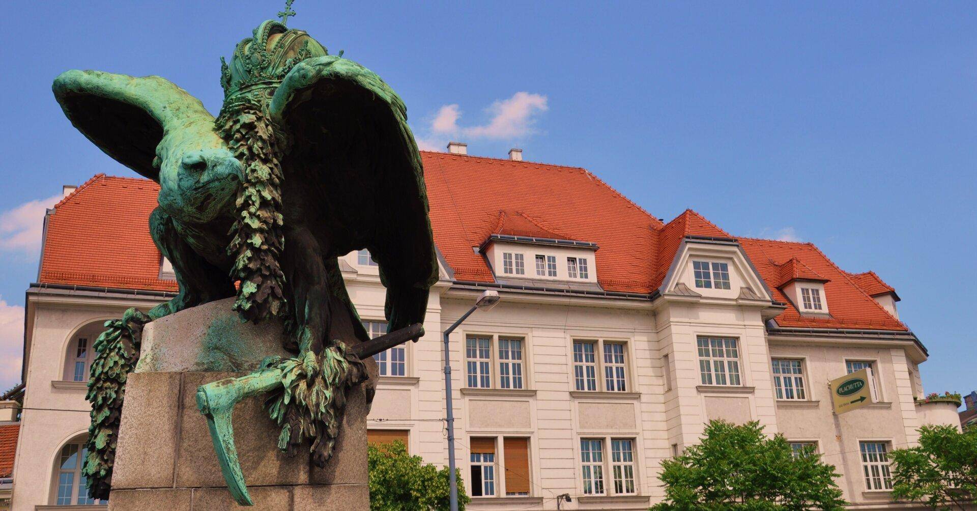 Historisches Gebäude mit rotem Ziegeldach und vielen Fenstern, teilweise verdeckt von einer großen grünen Statue.
