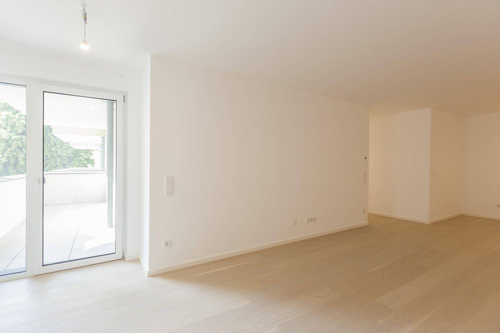 Offener, heller Wohnbereich mit Holzboden und Zugang zum Balkon.
