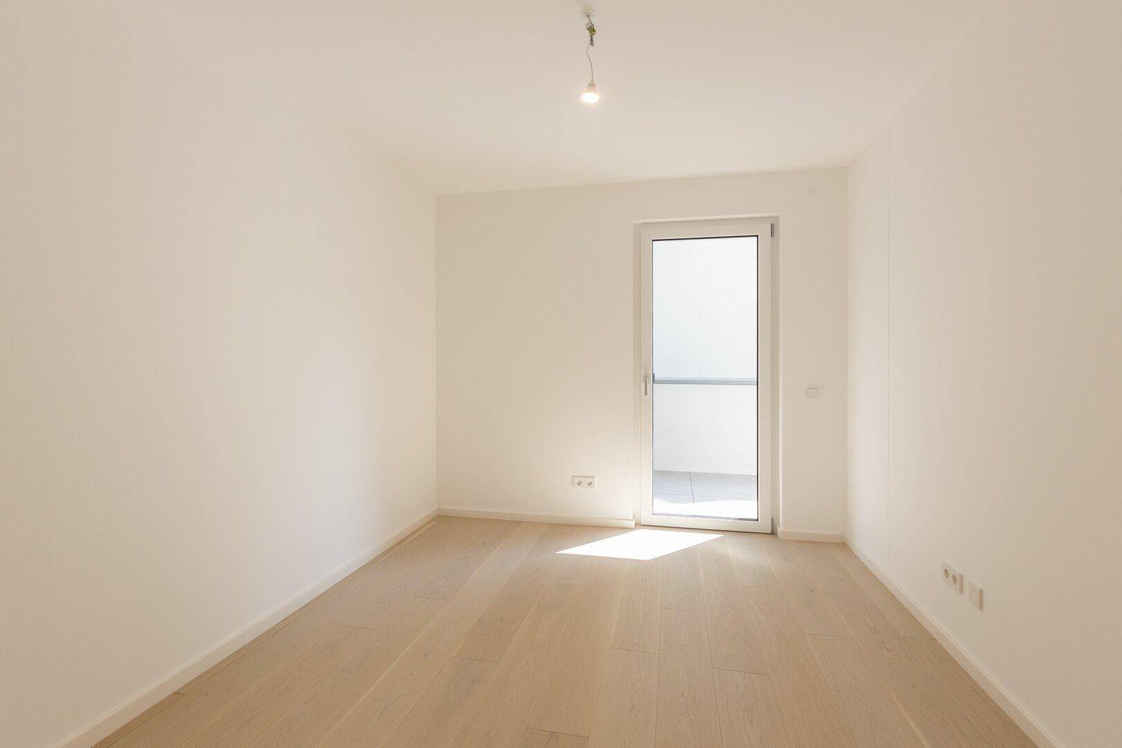 Leeres Schlafzimmer mit Holzboden und Zugang zu einem kleinen Balkon.