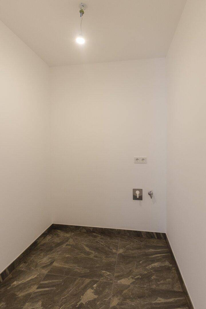 Kleiner Raum mit Fliesenboden und Anschlüssen für Waschmaschine oder Spüle.