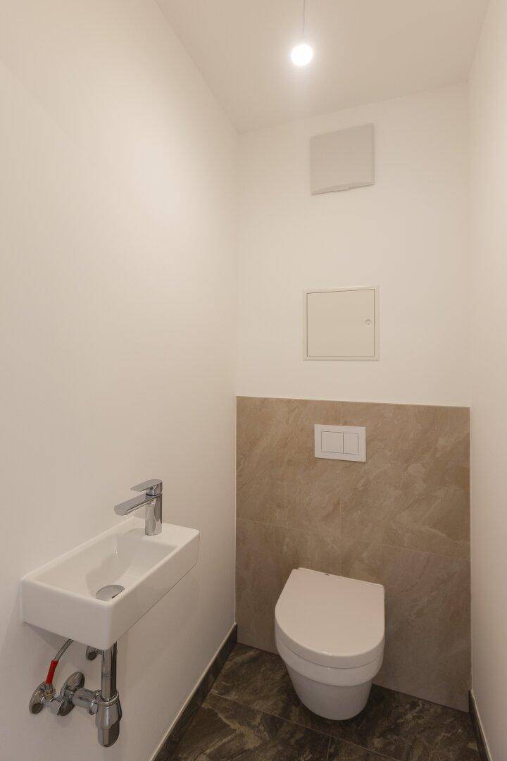 Gäste-WC mit wandhängender Toilette und kleinem Handwaschbecken.
