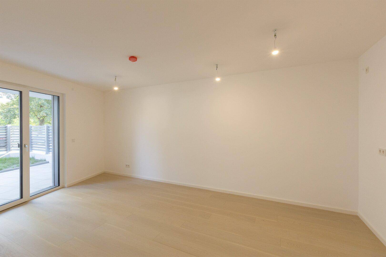 Heller, leerer Wohnraum mit hellem Holzfußboden und großem Zugang zur Terrasse.