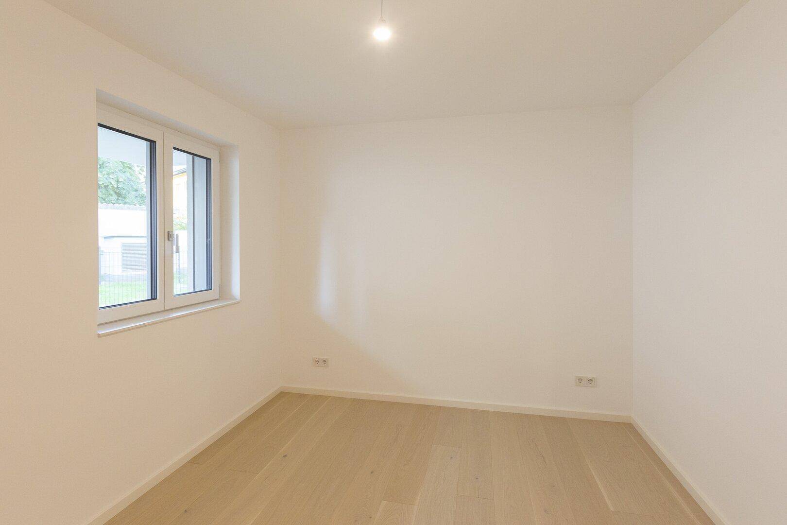 Helles, unmöbliertes Schlafzimmer mit Parkettboden und einem großen Fenster.