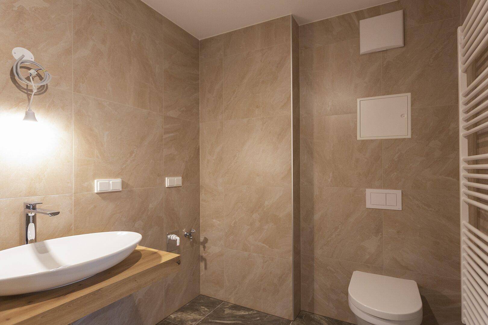Modernes Badezimmer mit beigefarbenen Fliesen, elegantem Waschbecken und Handtuchheizkörper.