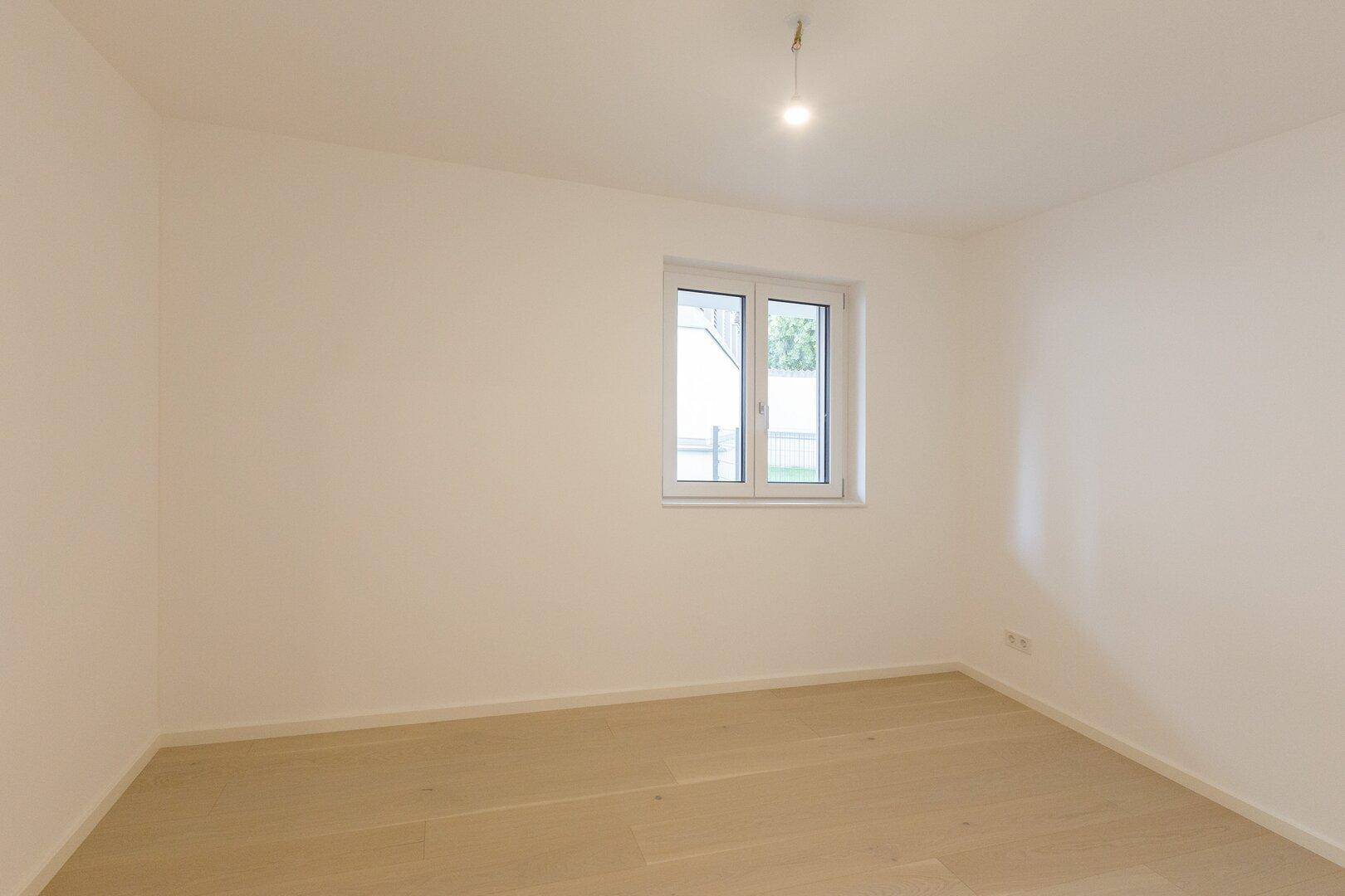 Unmöbliertes Schlafzimmer mit hellem Holzfußboden und viel Tageslicht durch das Fenster.