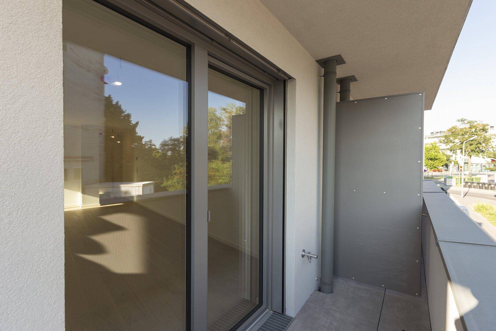 Nahaufnahme einer Glasschiebetür, die zu einem Balkon mit Sichtschutz und Fliesenboden führt.