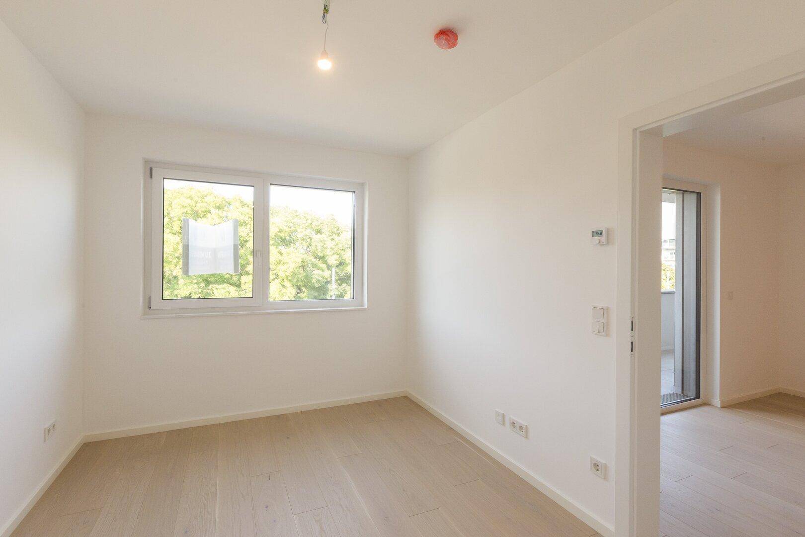 Helles Schlafzimmer mit Holzboden und Fenster mit Blick ins Grüne.