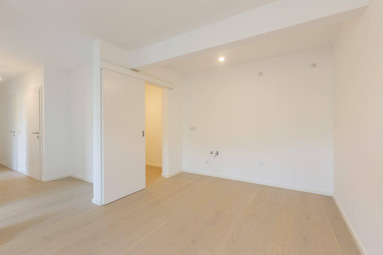 Leerer Raum mit Holzboden und Anschlüssen für eine zukünftige Küche.