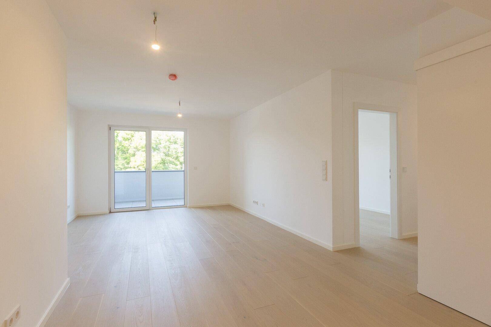 Heller, leerer Raum mit hellem Holzboden und Zugang zu einem Balkon.