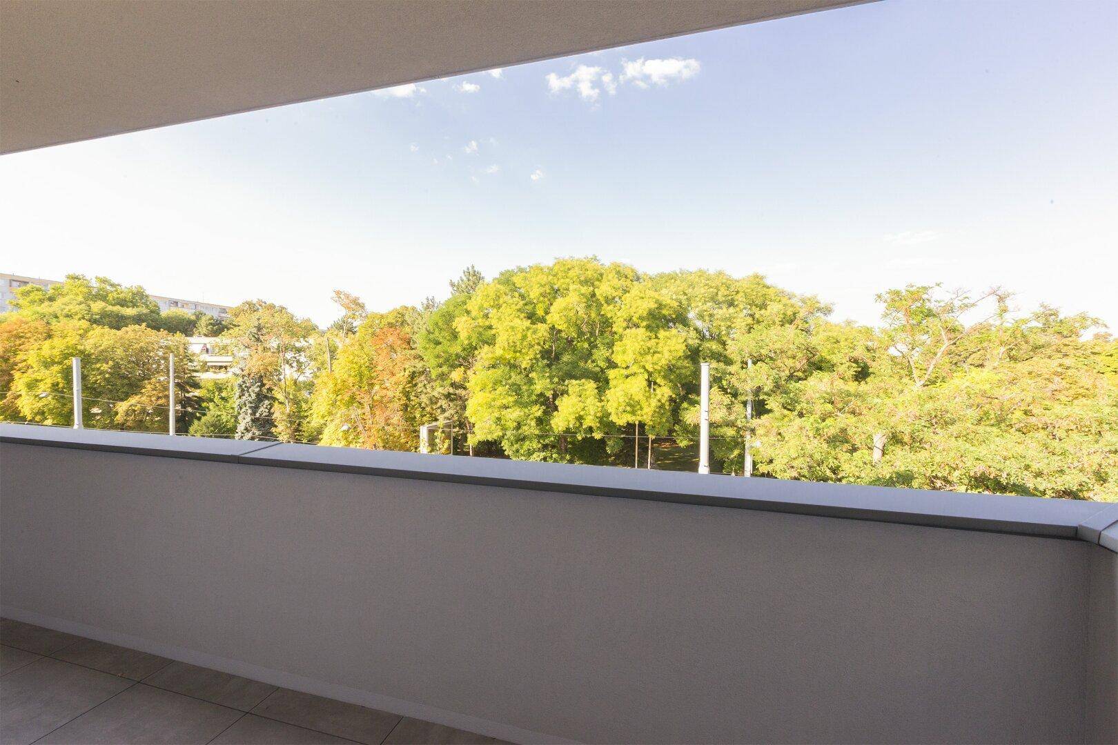 Weitläufiger Blick von einem Balkon auf üppiges Grün und den blauen Himmel.