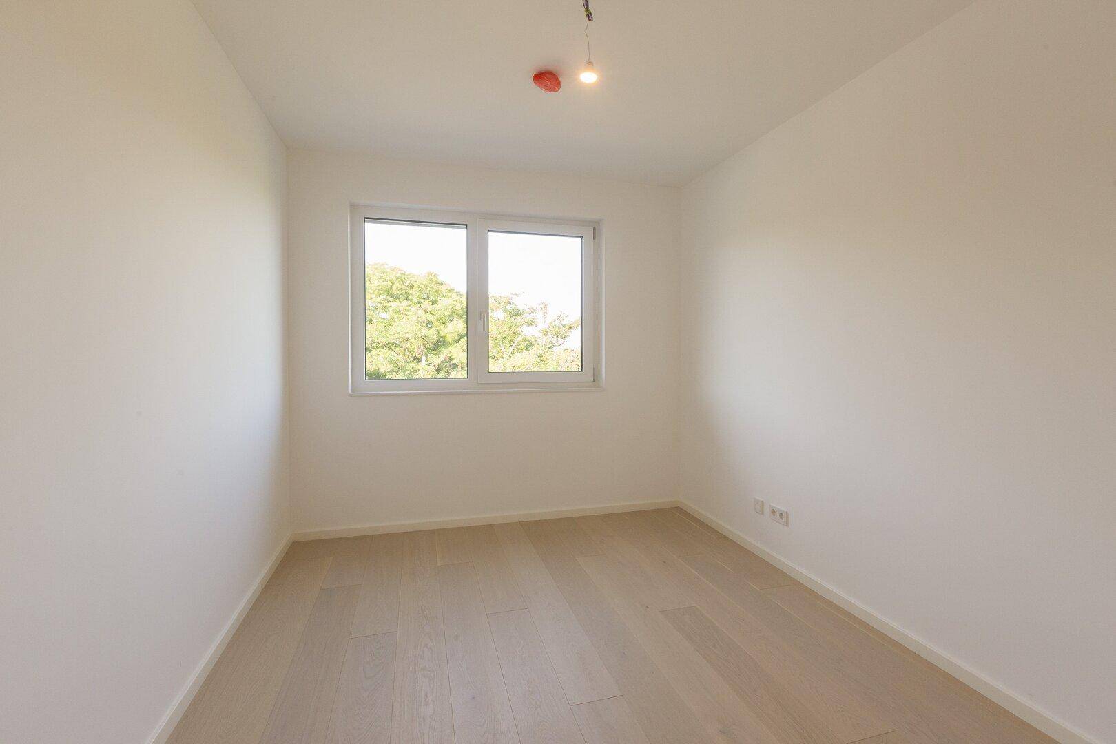 Gemütliches Schlafzimmer mit hellem Holzboden und einem Fenster mit Grünblick.