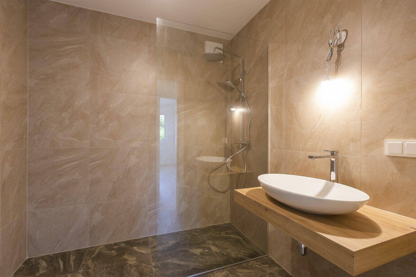 Modernes Badezimmer mit begehbarer Dusche, stilvollem Waschbecken und Holzwaschtisch.