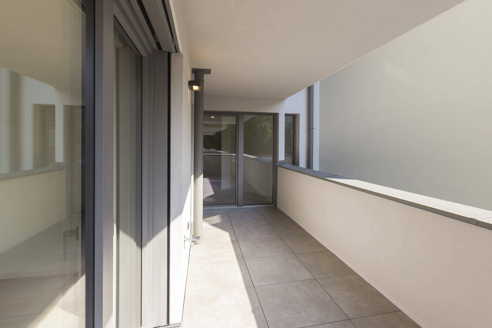 Schmaler, gefliester Balkon mit modernen Schiebetüren und viel Sonnenlicht.