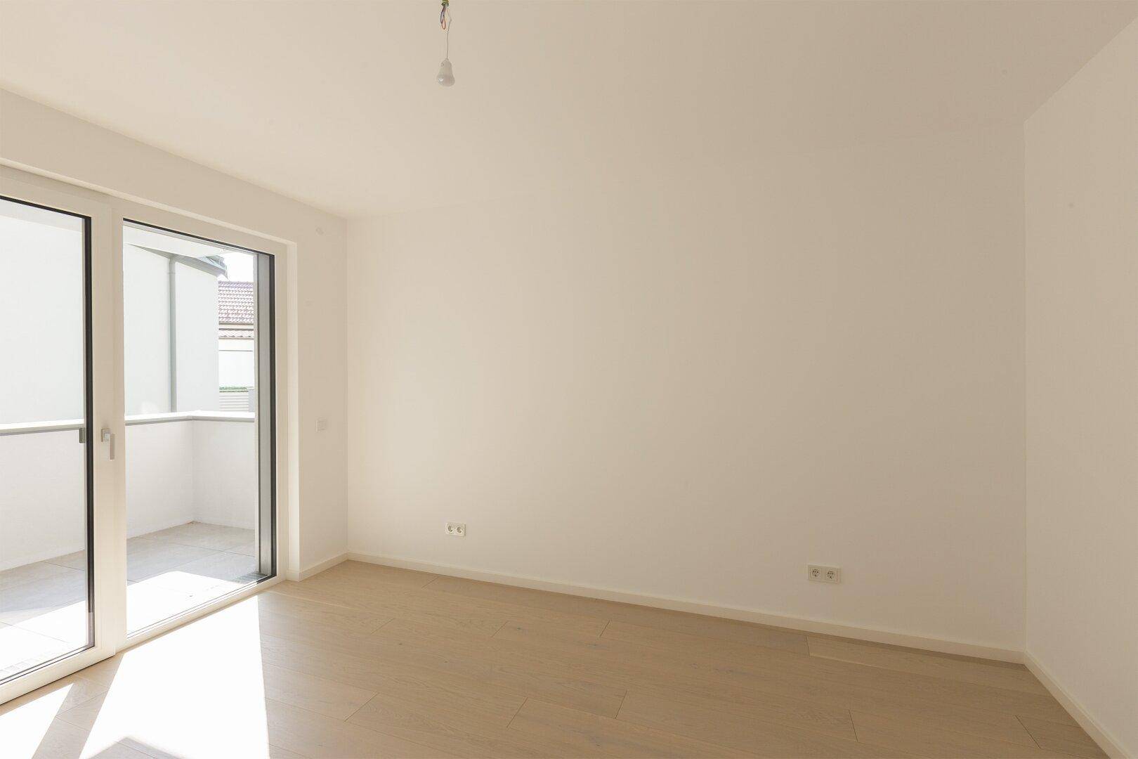 Lichtdurchflutetes Schlafzimmer mit Holzboden und großem Zugang zum Balkon.